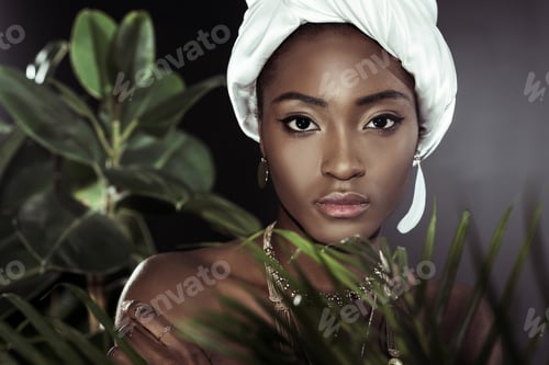 Preview: young african american woman in fashionable wire head wrap behind leaves