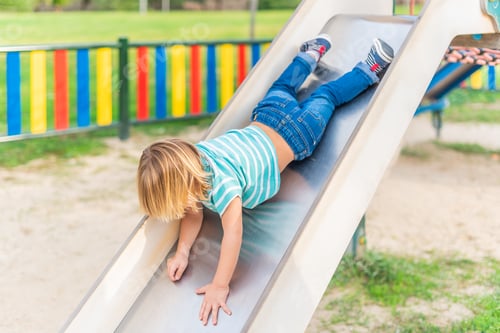 Preview: An unrecognizable little boy having fun while sliding on playground.