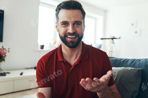 Preview: Handsome young man in casual clothing looking at camera and smiling while spending time indoors