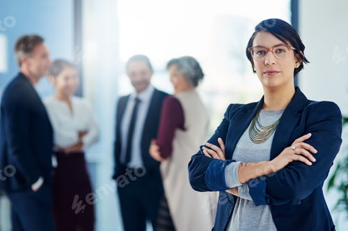 Preview: Cropped shot of a businesswoman standing with her arms crossed and her colleagues in the background