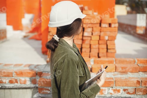 Preview: Stylish woman architect in hardhat with tablet and digital blueprints at construction site