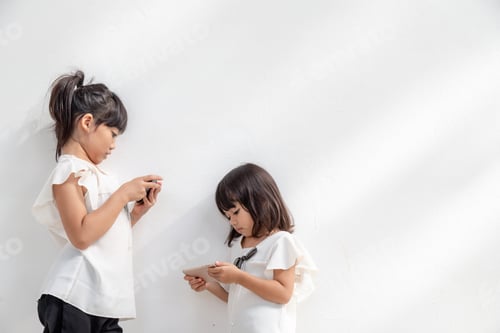 Vista previa: Niñas hermanas mirando sus teléfonos inteligentes sobre fondo blanco. Concepto social sobre la nueva tecnología