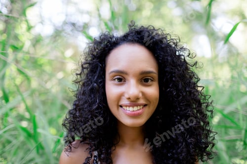 Preview: portrait outdoors of a beautiful young afro american woman at sunset. Green background. Lifestyle