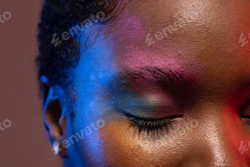 Preview: Close up of african american woman with short hair and colourful make up with eye closed