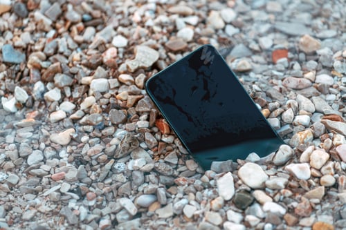 Preview: Lost smart phone device in pebbles on seaside beach in summer morning