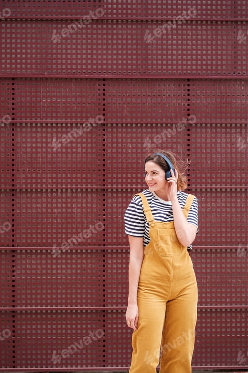 Preview: Woman in a yellow dress with a red background listening to music and dancing outdoors.