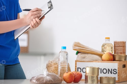 Preview: Female volunteer listing food products from donation box indoors
