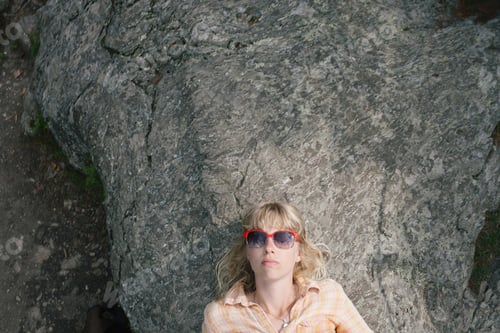 Preview: Young woman in sunglasses, lying on rock