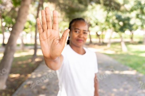Preview: African American woman raising hand to signal stop in park, confident expression