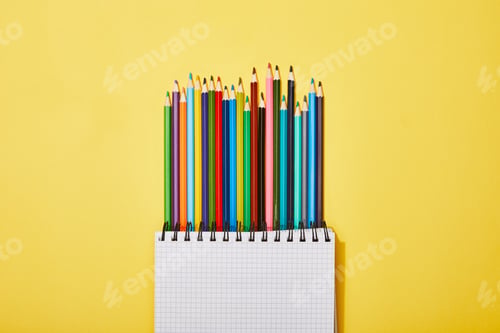 Preview: top view of colored pencils near blank notebook on yellow