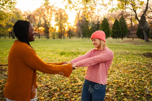 Preview: Diverse women friends holding hands playing in autumn park