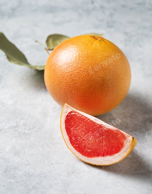 Preview: Juicy red grapefruit with slice and green leaf on a blue background close up.