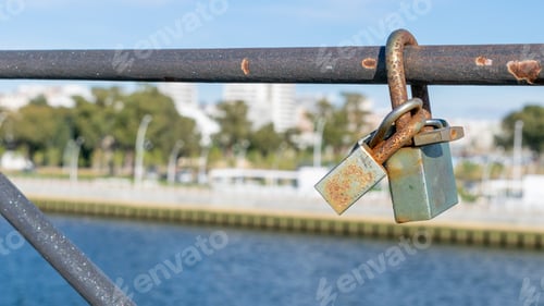 Preview: Closeup shot of rusty locks on metallic handrails under the sunlight with a river on the background