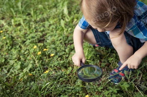 Preview: Happy little boy exploring nature with magnifying glass at the day time