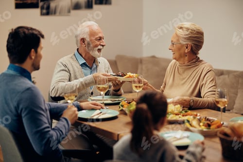 Visualização: Casal sênior feliz passando comida durante o almoço em família na mesa de jantar.