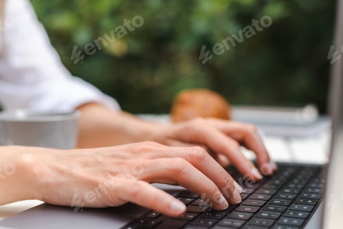 Preview: Unrecognizable female hands are typing on a laptop keyboard during a business meeting in a cafe.