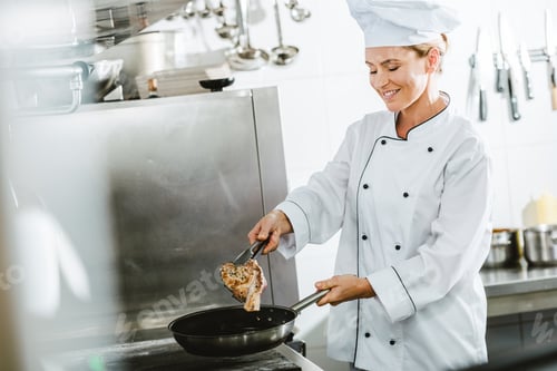 Preview: beautiful smiling female chef in uniform cooking meat in restaurant kitchen