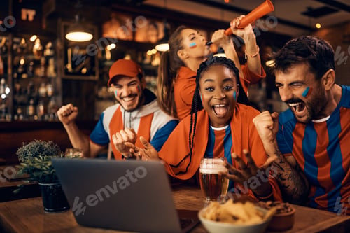 Preview: Excited sports fans celebrating favorite team's victory while watching match on laptop in pub.
