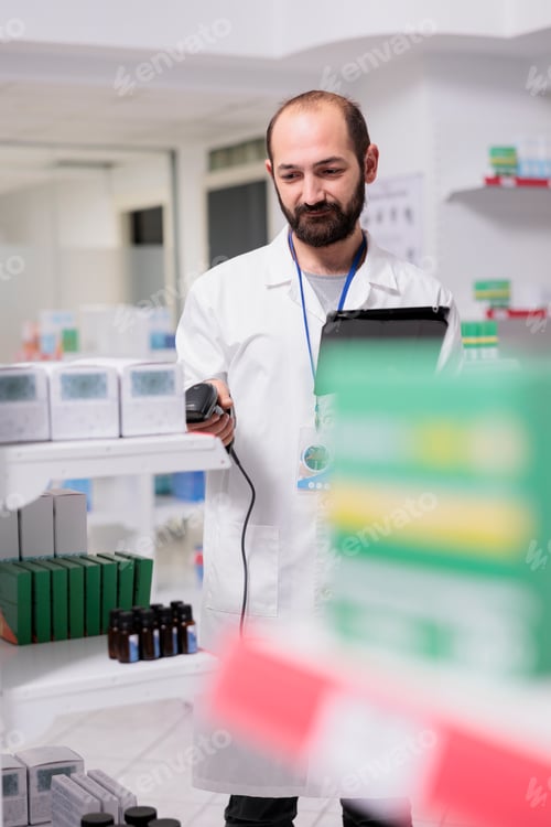 Preview: Portrait of pharmacist checking medication list on tablet computer while scanning pills packages