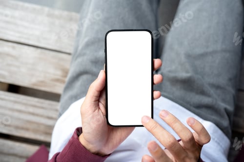 Preview: A man's hands holding blank screen smartphone with fingers hovering sitting outdoor on wooden bench.