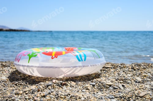 Preview: inflatable swimming children circle lies on the pebble beach on the background of water