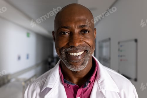 Preview: Portrait of happy african american male doctor wearing lab coat in corridor at hospital