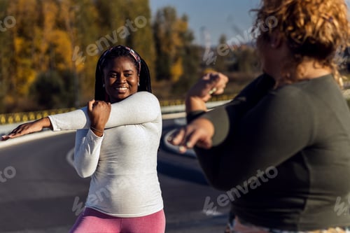 Preview: Two young plus size women stretching together before running.