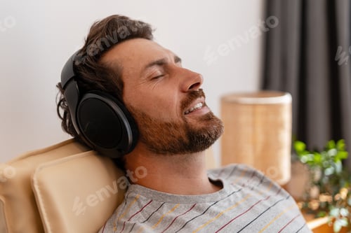 Preview: Man relaxing on armchair listening to music with headphones