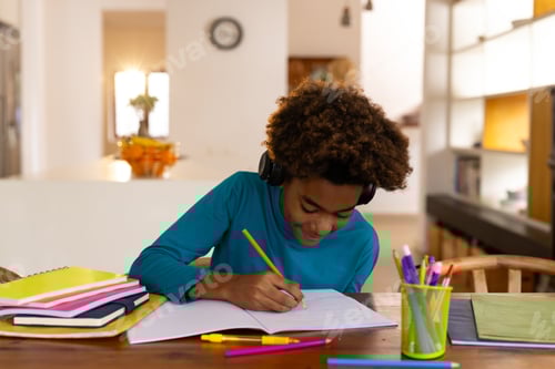 Preview: Happy african american boy sitting at table having online class and taking notes