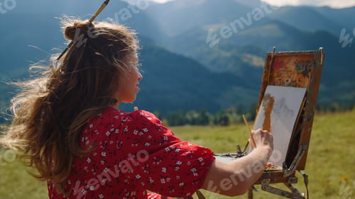 Preview: Woman painter drawing mountains landscape on meadow. Girl painting using easel.