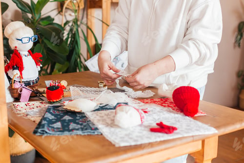 Preview: female hands make handmade dolls on the background of multicolored fabric, scissors