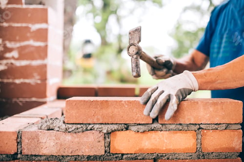 Preview: industrial worker building exterior walls, using hammer for laying bricks in cement