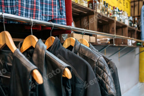 Preview: Second hand black leather vests and jackets in hangers on vintage clothes shop with copy space