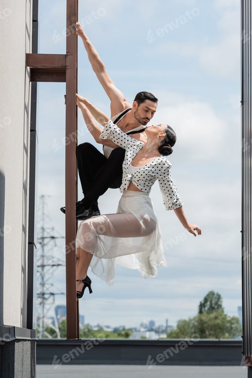 Preview: Professional dancers kissing while posing on ladder on rooftop of building at daytime