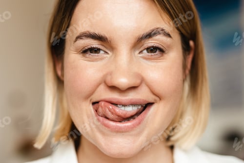 Preview: Young woman smiling while licking her brace indoors