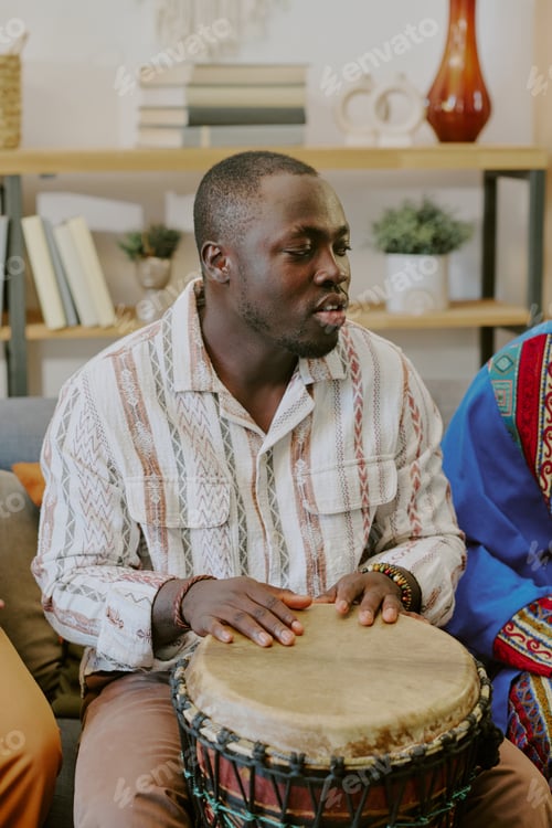 Preview: Young Adult Black Man Playing Drum during Kwanzaa Celebration Indoors