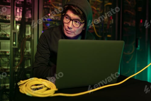 Preview: Asian male hacker using a laptop in computer server room