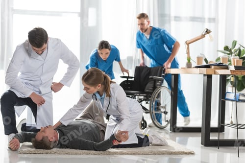 Preview: young doctors checking pulse of unconscious man lying on a floor in hospital
