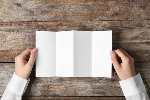 Preview: Woman holding blank brochure mock up on wooden table, top view