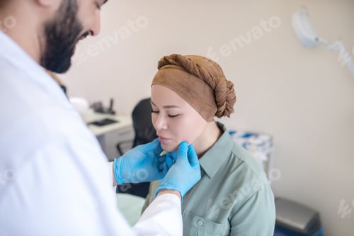 Preview: Tall doctor in blue gloves examining his female patient