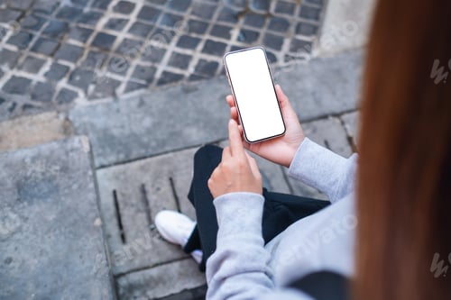 Preview: Top view mockup image of a woman holding mobile phone with blank white screen in the outdoors