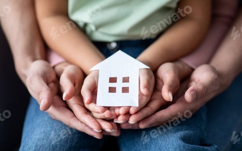 Preview: Man, woman and little child holding cutout paper house figure in hands