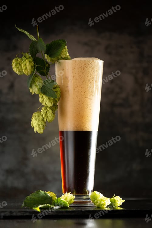 Preview: Glass of dark beer with hops around on a dark background