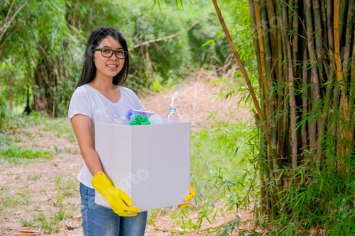 Preview: Lovely Asian teen girl with white t-shirt and glasses holds white box filled with plastic