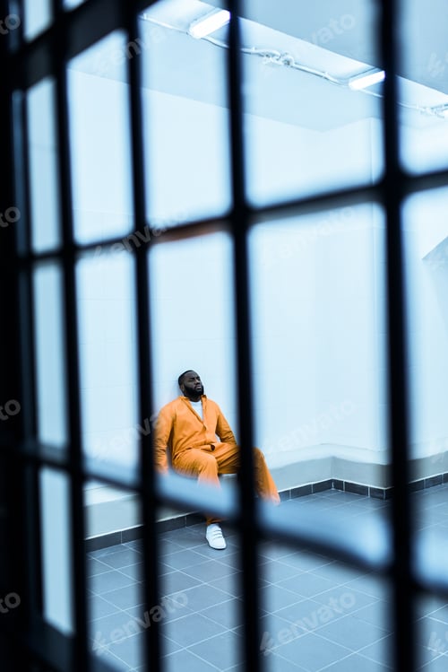 Preview: african american prisoner sitting on bench in prison cell