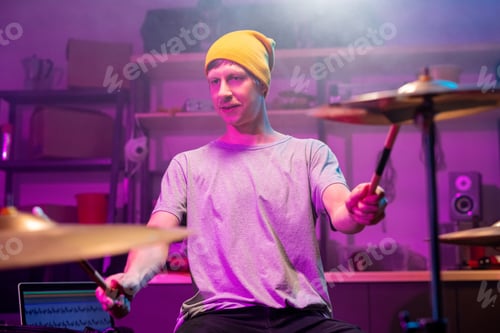 Preview: Contemporary young musician in casualwear touching cymbals with drumsticks