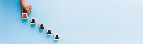 Preview: partial view of hand and wooden blocks with black and red human icons on blue background, leadership