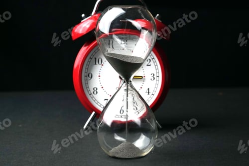 Preview: Glass hourglass and an old-fashioned alarm clock depicting the passage of time