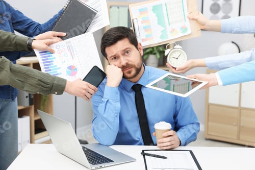 Preview: Man overwhelmed by different requests from colleagues at desk in office