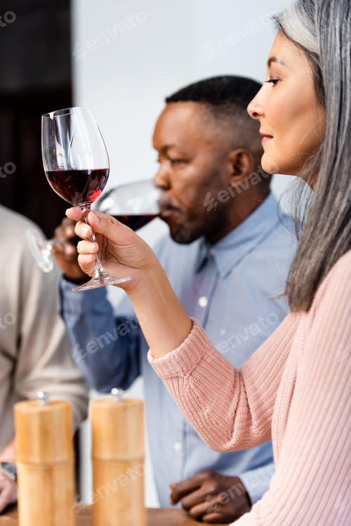 Preview: selective focus of asian woman looking at wine glass and african american man drinking wine